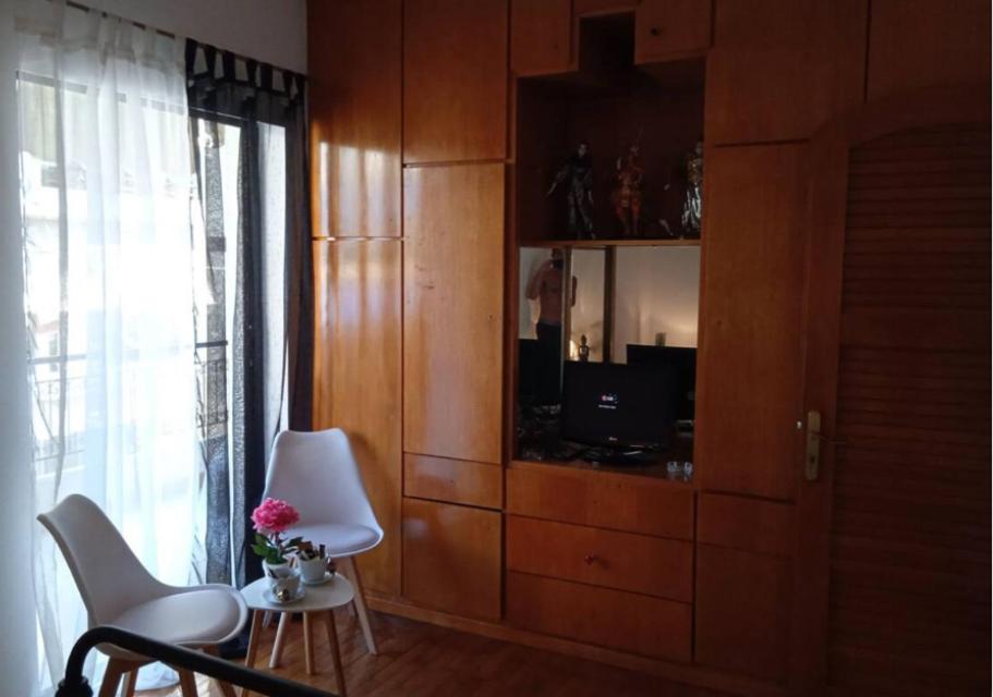 a living room with a cabinet with a tv and white chairs at Nicko’s room in Piraeus