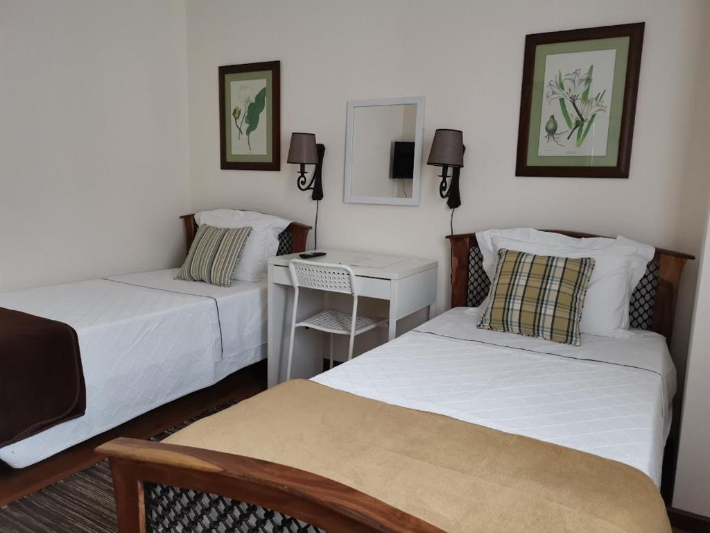 two beds in a room with a desk and a bed at Casa das Palmeiras in São Vicente Ferreira