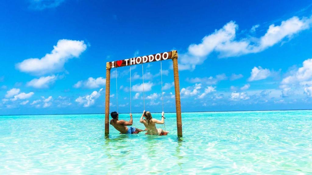 un hombre y una mujer sentados en el agua en el océano en Blue Coral Thoddoo, en Thoddoo