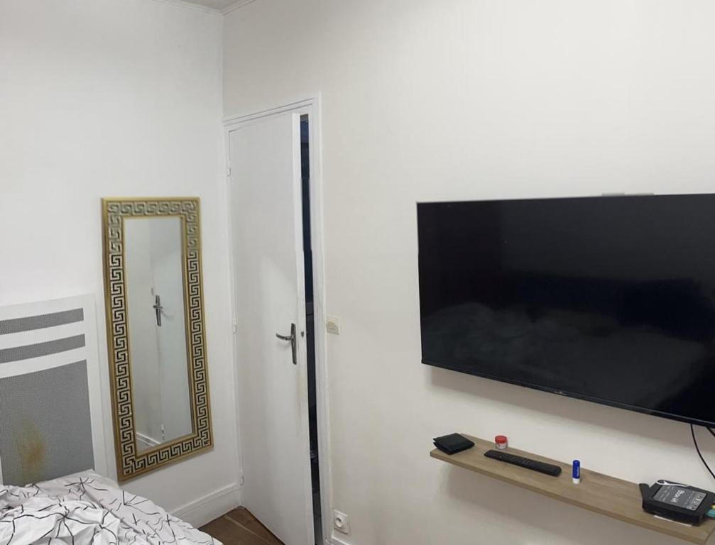 a flat screen tv on a wall with a mirror at chambre d'hote in Issy-les-Moulineaux