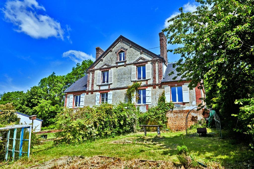 ein altes Backsteinhaus mit blauen Fenstern auf einem Hügel in der Unterkunft Charmant presbytère en Basse-Normandie in Crouttes