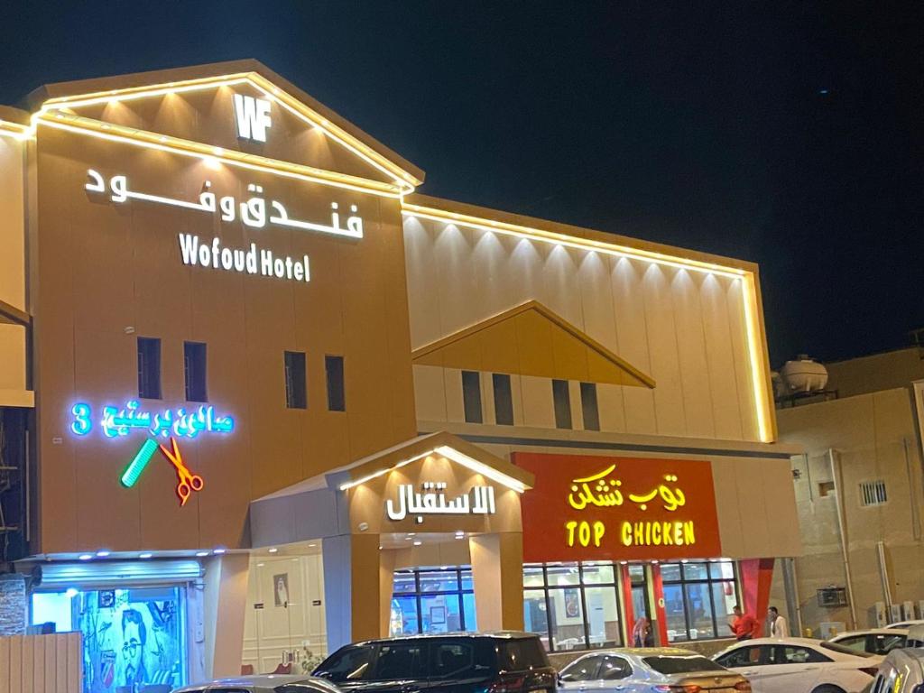 a building with neon signs and cars parked in front of it at فندق وفود in Rafha