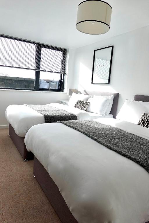 1 Schlafzimmer mit 3 Betten mit weißer Bettwäsche und einem Fenster in der Unterkunft Modern Luxurious Apartment in Birmingham