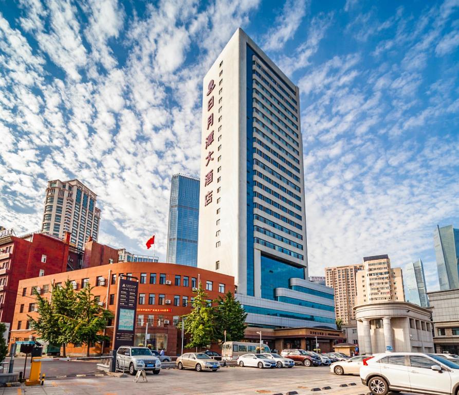 a tall building with cars parked in a parking lot at Sun Moon Lake Hotel Dalian大连火车站店 in Dalian