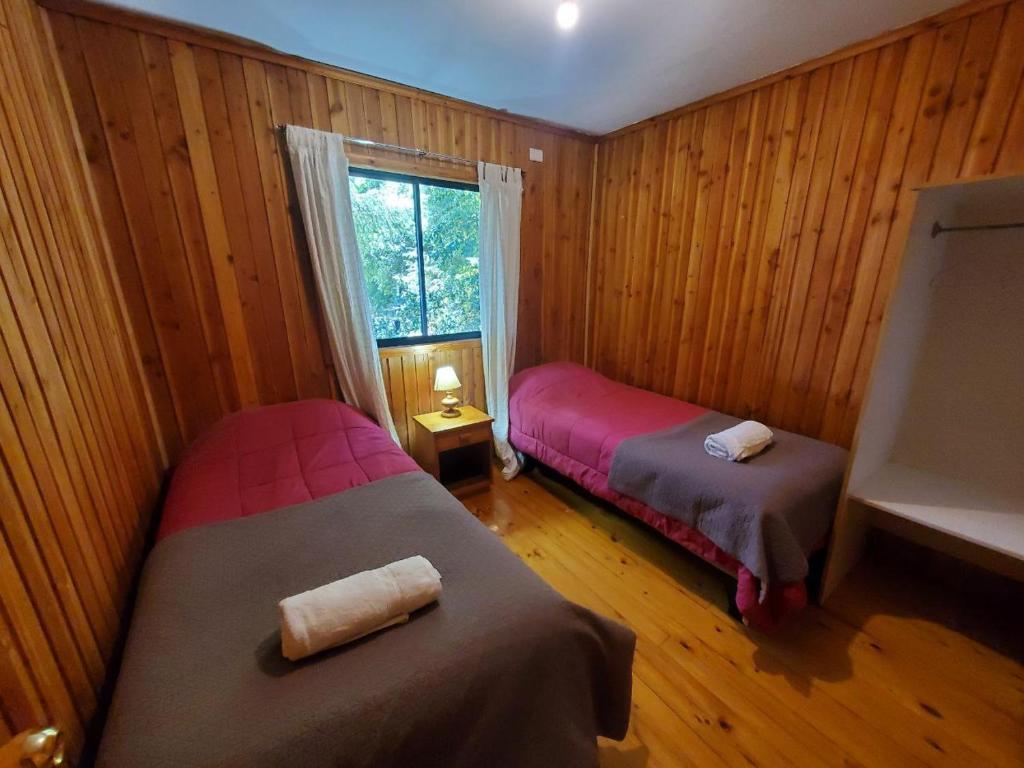 two beds in a room with wooden walls and a window at Cabaña en las afueras de Panguipulli in Panguipulli