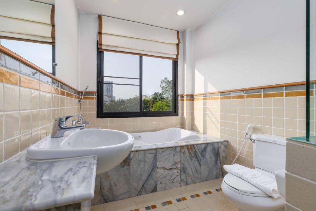 A tiled bathroom combines a freestanding-style bathtub, pedestal sink, toilet, and window.