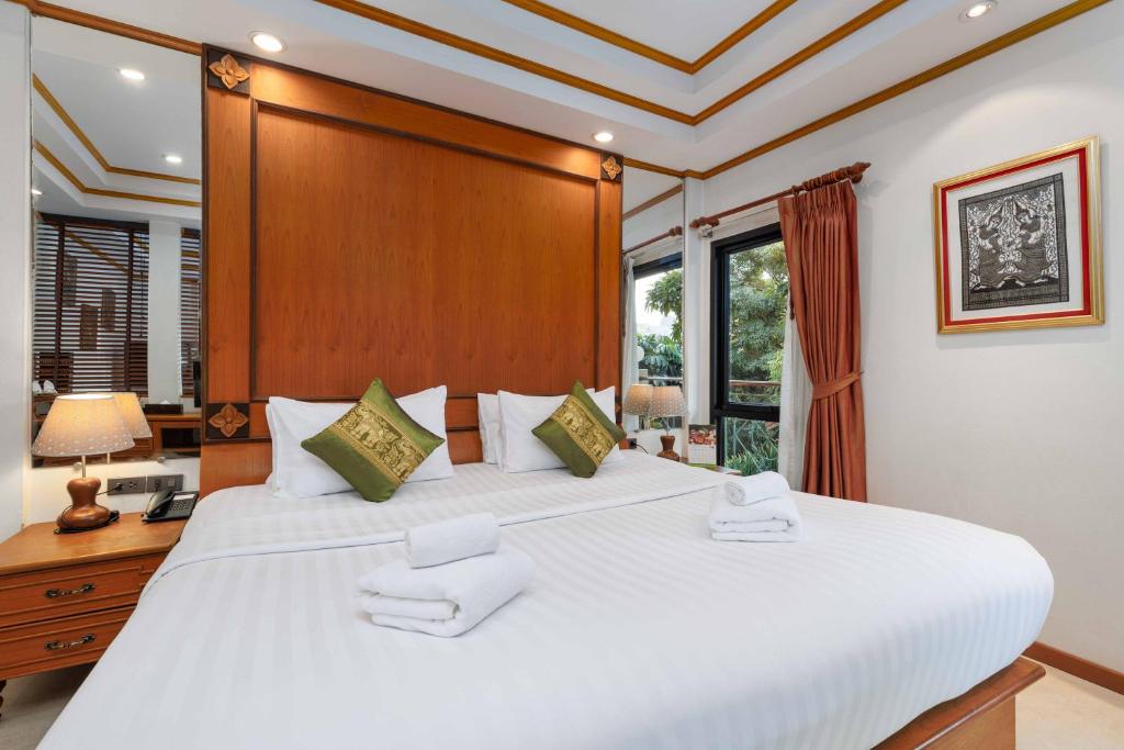 A neatly made traditional bedroom with a large bed, bedside lamp and leafy window outlook.
