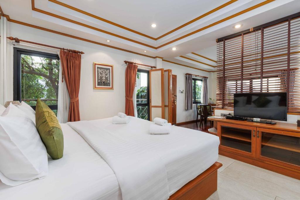 A large bedroom pairs a white bed with a television and several windows.