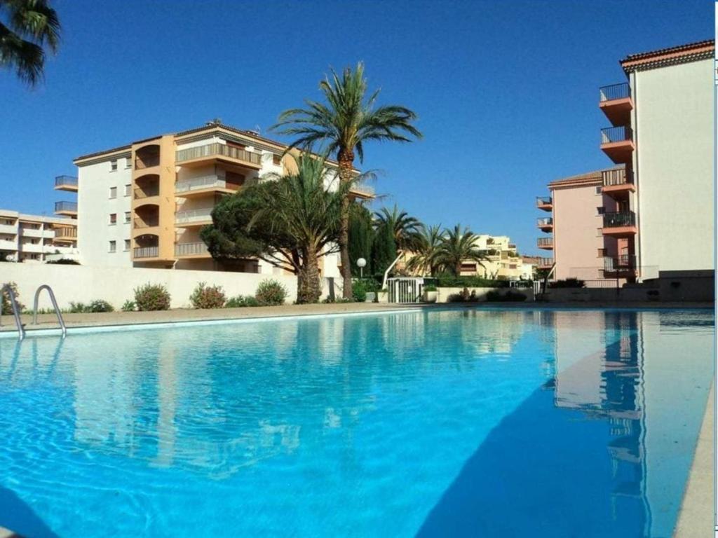 ein großer Swimmingpool mit Palmen und Gebäuden in der Unterkunft Appartement 2P climatisé avec WIFI, piscine, parking privé, proche plages et centre Sainte-Maxime - FR-1-780-1 in Sainte-Maxime