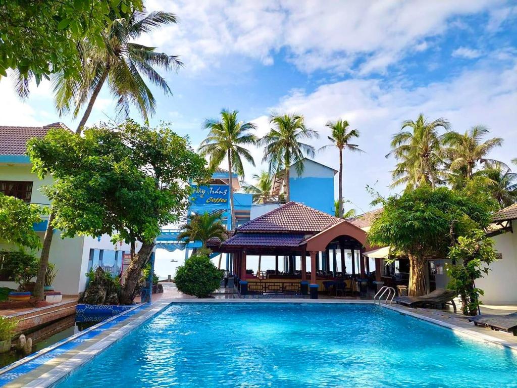 einem Pool vor einem Gebäude mit Palmen in der Unterkunft Sóng Biển Xanh Mũi Né Resort - by Bay Luxury in Ấp Long Sơn