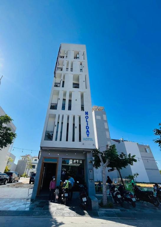 a tall white building with people standing outside of it at HOLIDAY HOTEL PHAN THiẾT in Ấp Bình Hưng