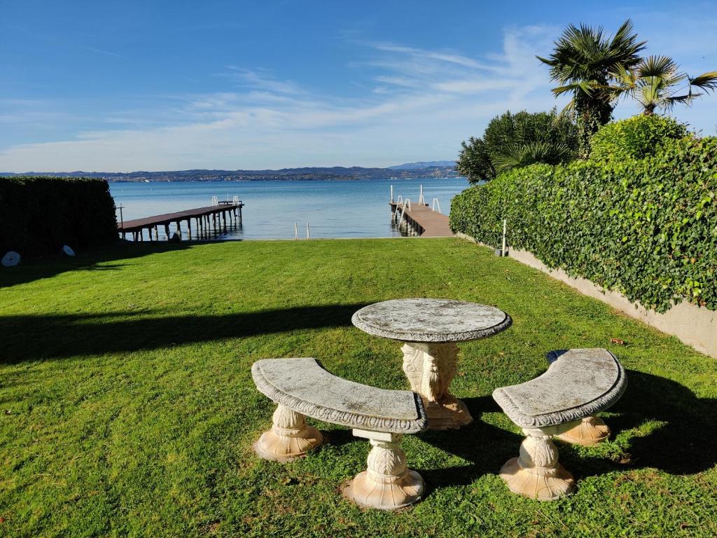 zwei Steinbänke auf dem Gras in der Nähe des Wassers in der Unterkunft Trilocale Sporting con giardino privato e WiFi - Sunset Beach in Sirmione