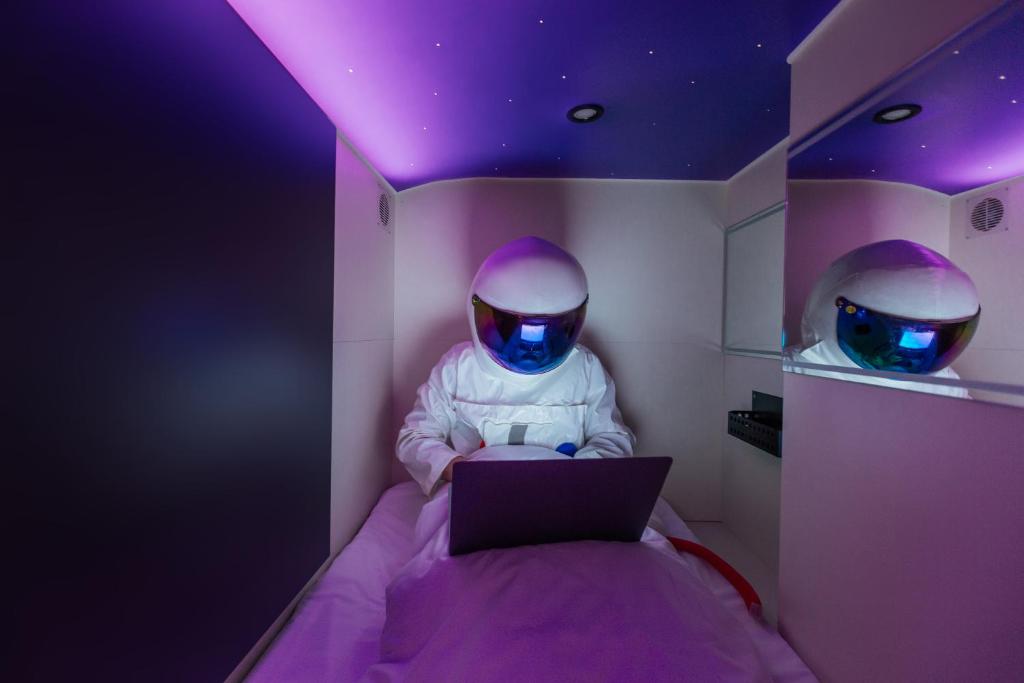 Capsule Hotel Constellation 91 في إلفيف: شخص في غرفة مع لاب توب على سرير