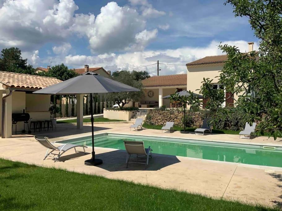 een patio met een parasol en stoelen en een zwembad bij Maison Provençale avec piscine in Sérignan-du-Comtat
