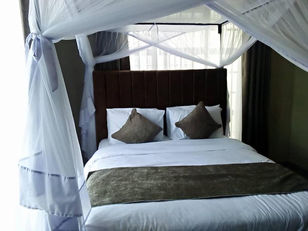 ein Schlafzimmer mit einem Himmelbett mit weißer Bettwäsche und Kissen in der Unterkunft FABRISSA HOMES in Arusha