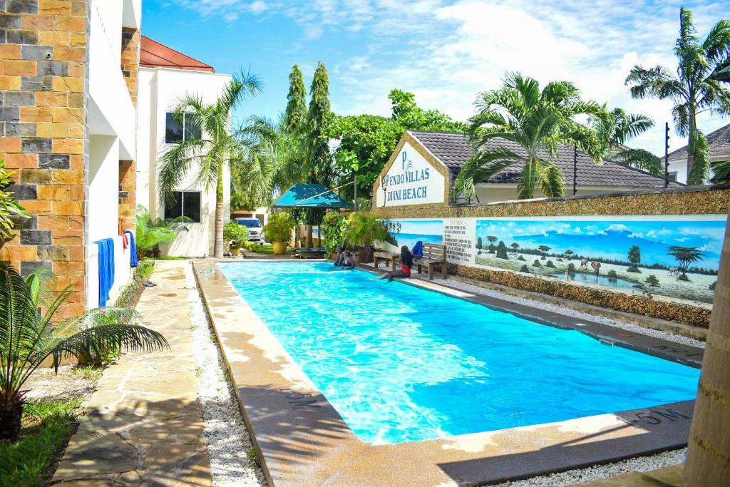a swimming pool with blue water in front of a building at Pendo Villas Diani Beach in Diani Beach