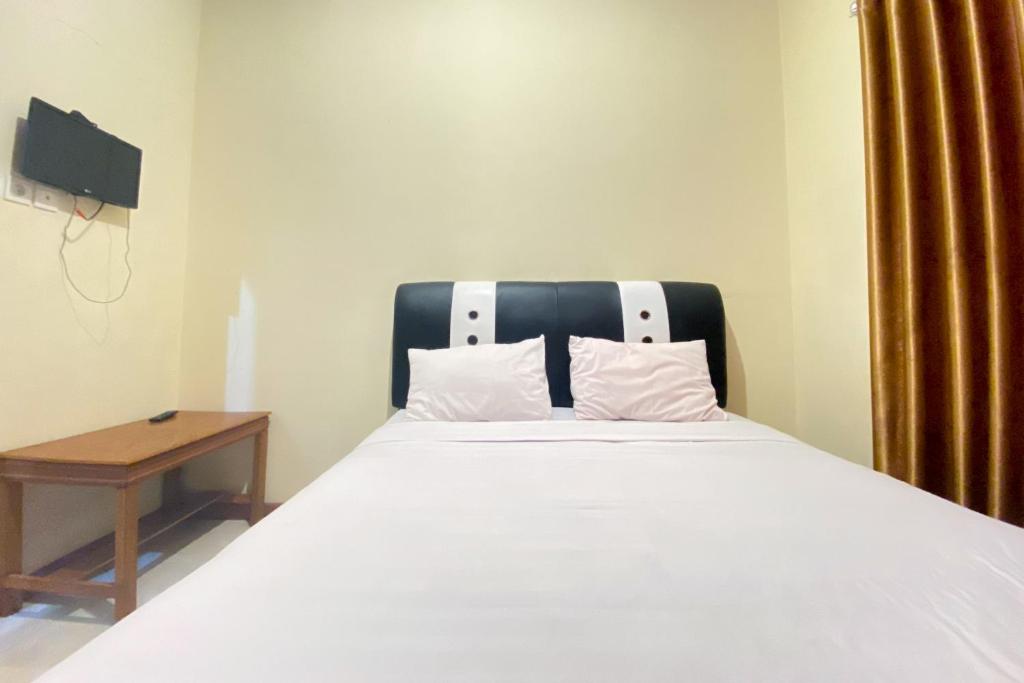 1 dormitorio con 1 cama blanca con cabecero negro y mesa en RedDoorz Syariah at D'Rizs Homestay en Bukittinggi