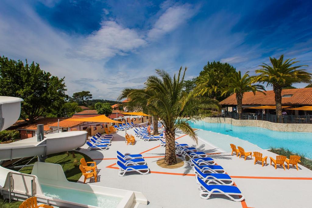 un complexe avec une piscine bordée de chaises et de palmiers dans l'établissement Camping Bela Basque - Maeva, à Anglet