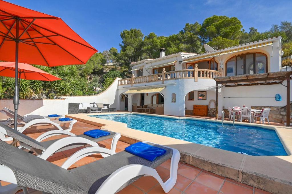 a house with a swimming pool with chairs and an umbrella at Casa Patricia in Jávea