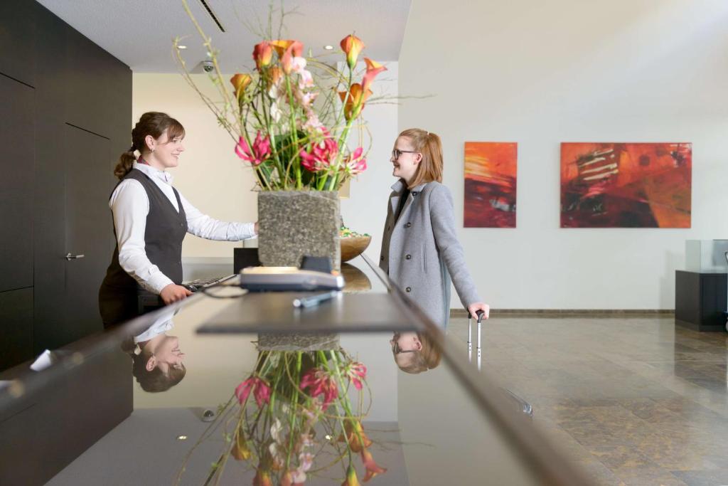 two women standing at a table with a vase of flowers at ATLANTIC Hotel Lübeck in Lübeck