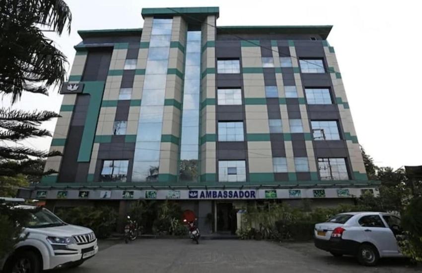 un grand bâtiment avec des voitures garées devant dans l'établissement Hotel Ambassador Chocolate Inn, à Kalyani