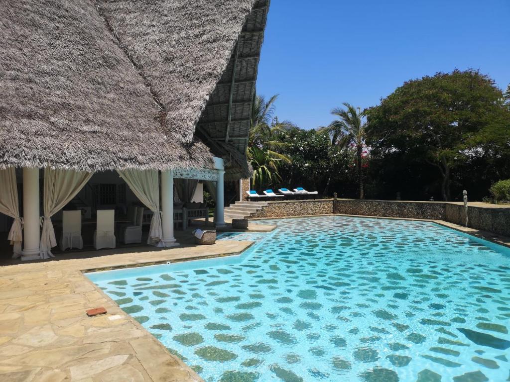 a resort swimming pool with a thatch roof at Fulvia House in Malindi