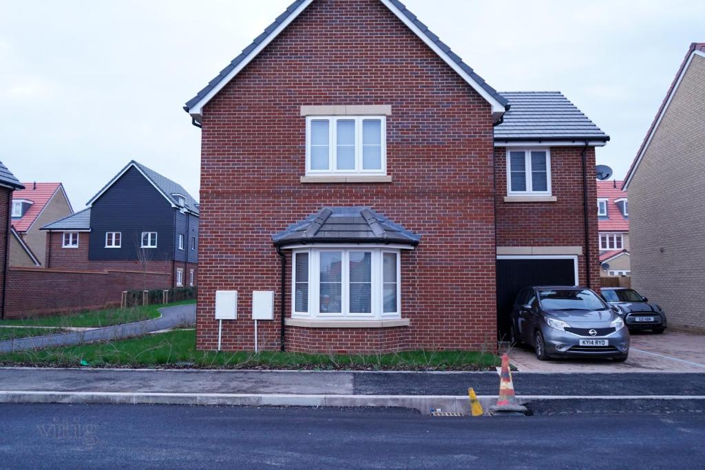una casa de ladrillo rojo con un coche aparcado delante de ella en A1M Hampton Lakes Brand New Entire House en Peterborough