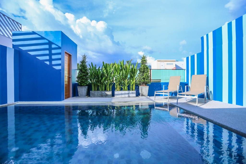 a swimming pool with two chairs and a blue building at Ocean and Ole Patong Hotel in Patong Beach