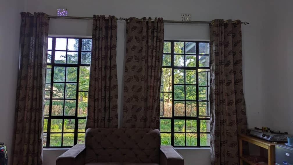 sala de estar con 2 ventanas grandes y sofá en Mwacha_Farm_house, en Moshi