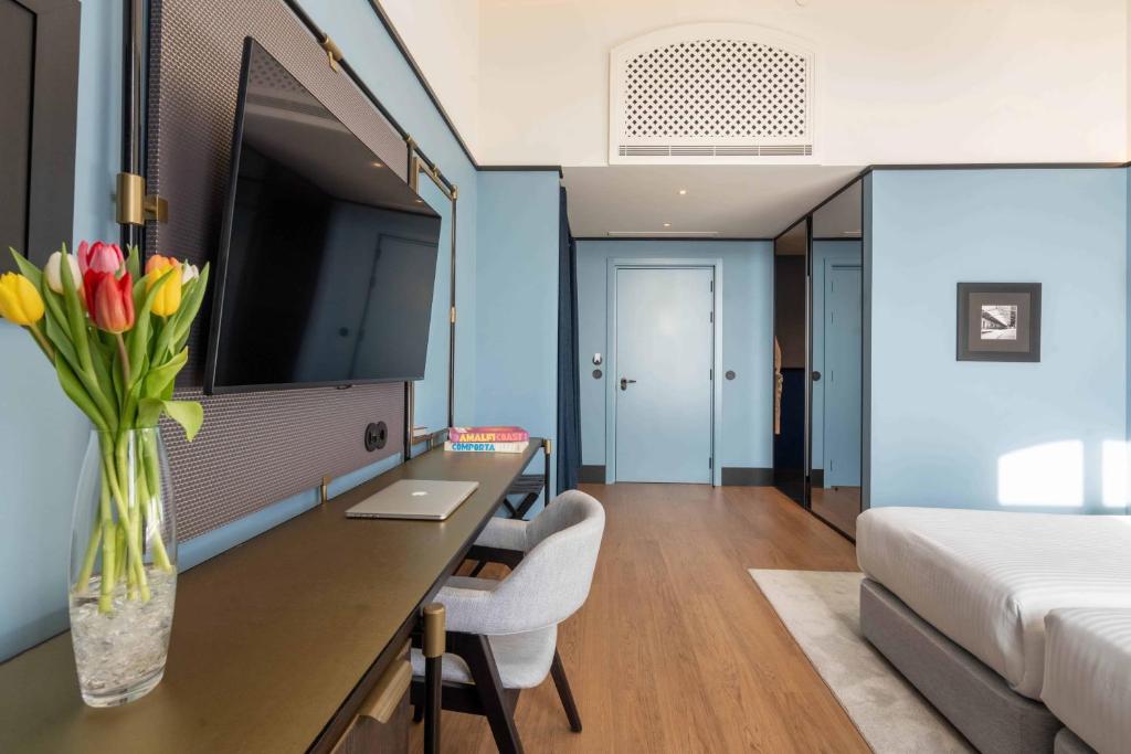 A blue-toned bedroom with a long work surface, television, and entry corridor.