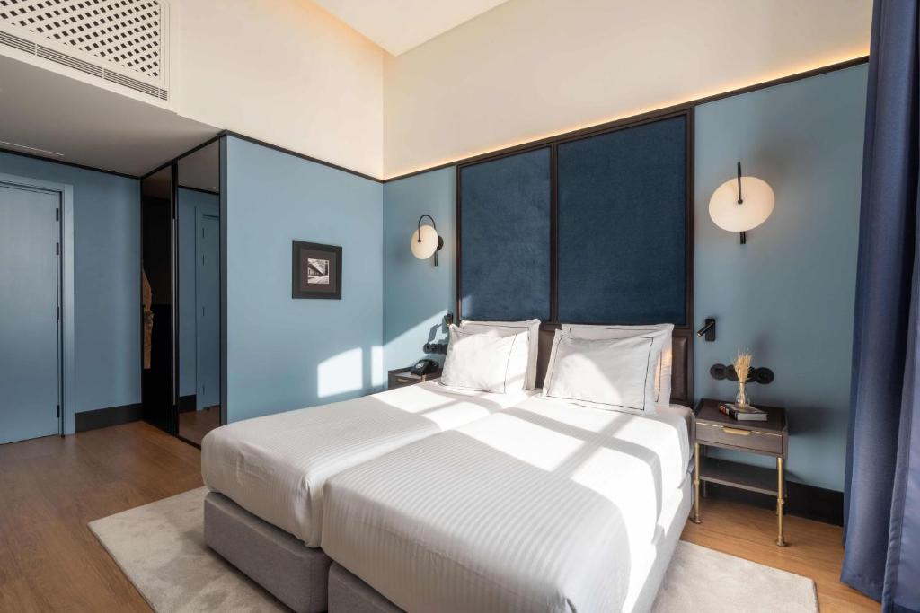 A compact twin room with two beds, blue walls, a blue headboard and bright window light.