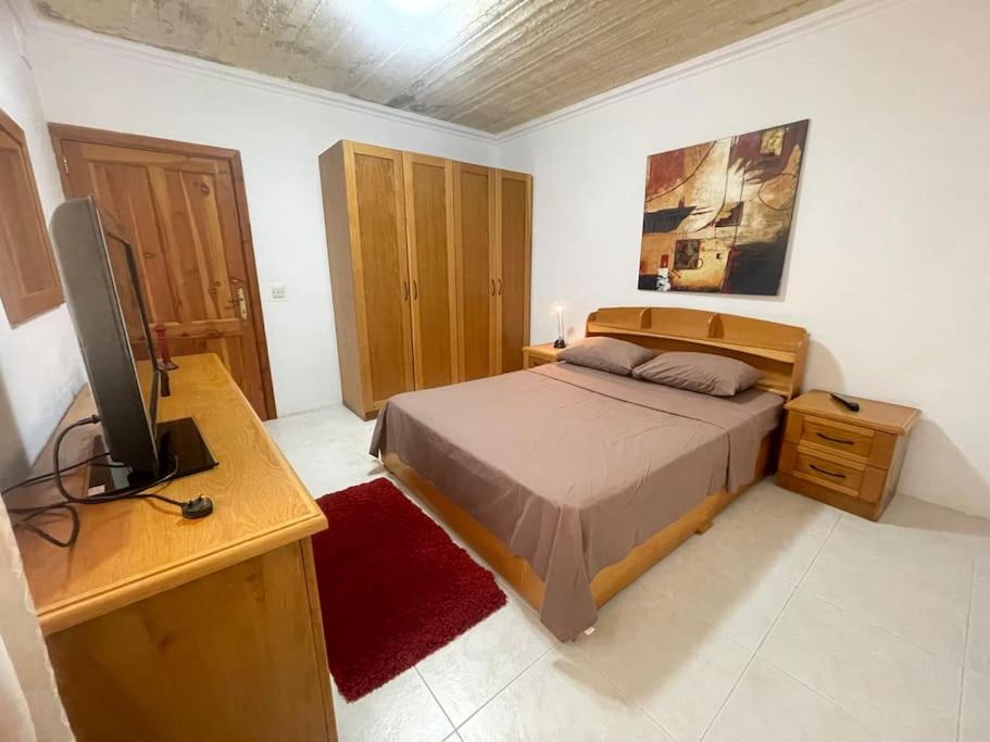 een slaapkamer met een bed, een bureau en een televisie bij Mellieha Apartment in Mellieħa