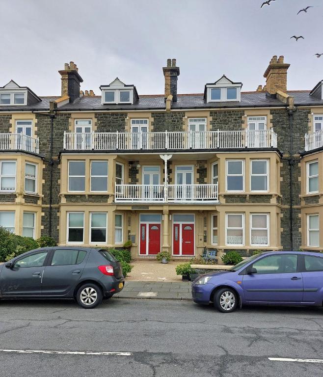 two cars parked in front of a large building at Trem Y Mor - Edge of the Sea in Tywyn