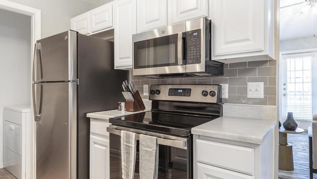 a kitchen with white cabinets and a stainless steel refrigerator at Landing Modern Apartment with Amazing Amenities (ID8521X55) in Fort Worth
