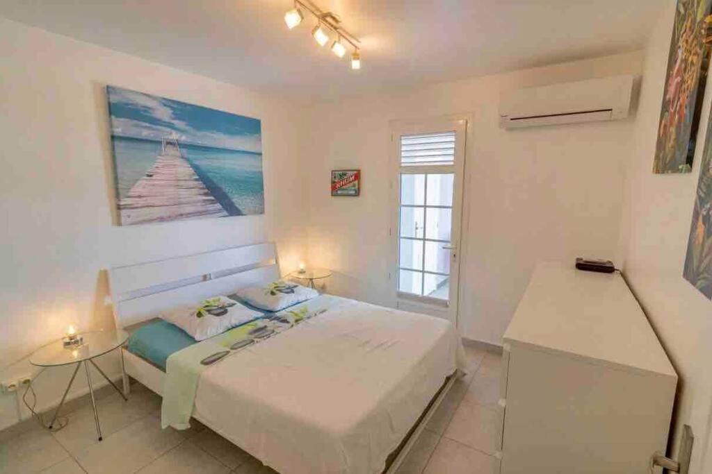a white bedroom with a bed and a window at Villa Ti Paradis in Sainte-Luce