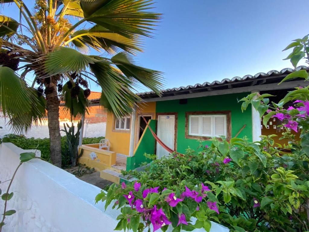 a green and yellow house with a palm tree and flowers at Pousada Brisa do Mar in Galinhos