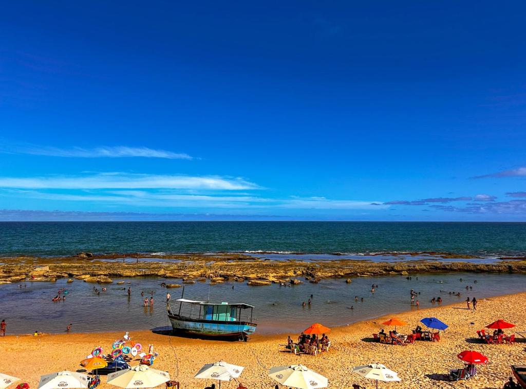 Kitnet beira mar com WiFi em Arembepe Camacari BA في كامساري: شاطئ فيه مظلات و قارب في الماء