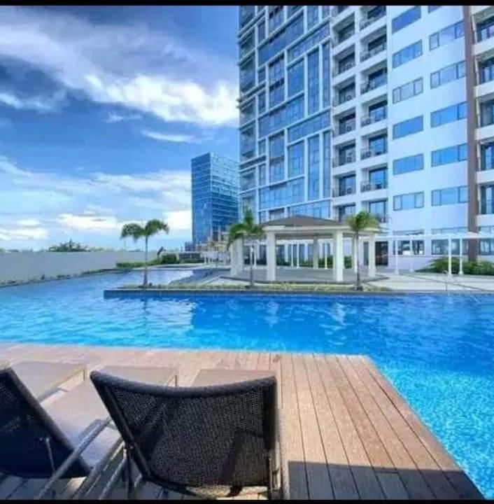 a large swimming pool with two chairs and a building at Mactan Newtown By The Beach in Lapu Lapu City