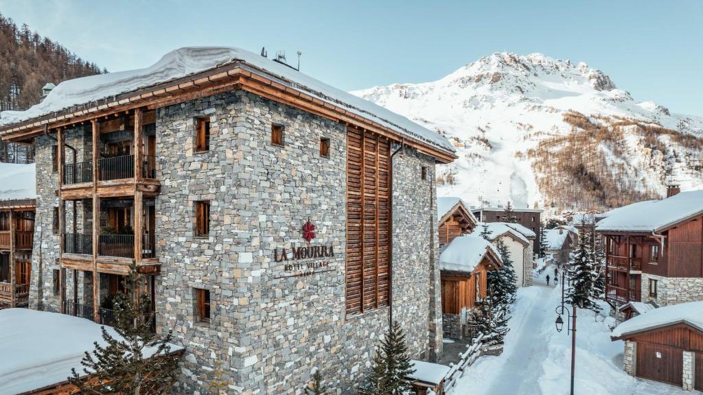 a building in the snow with a mountain in the background at Hôtel LA MOURRA in Val-d'Isère
