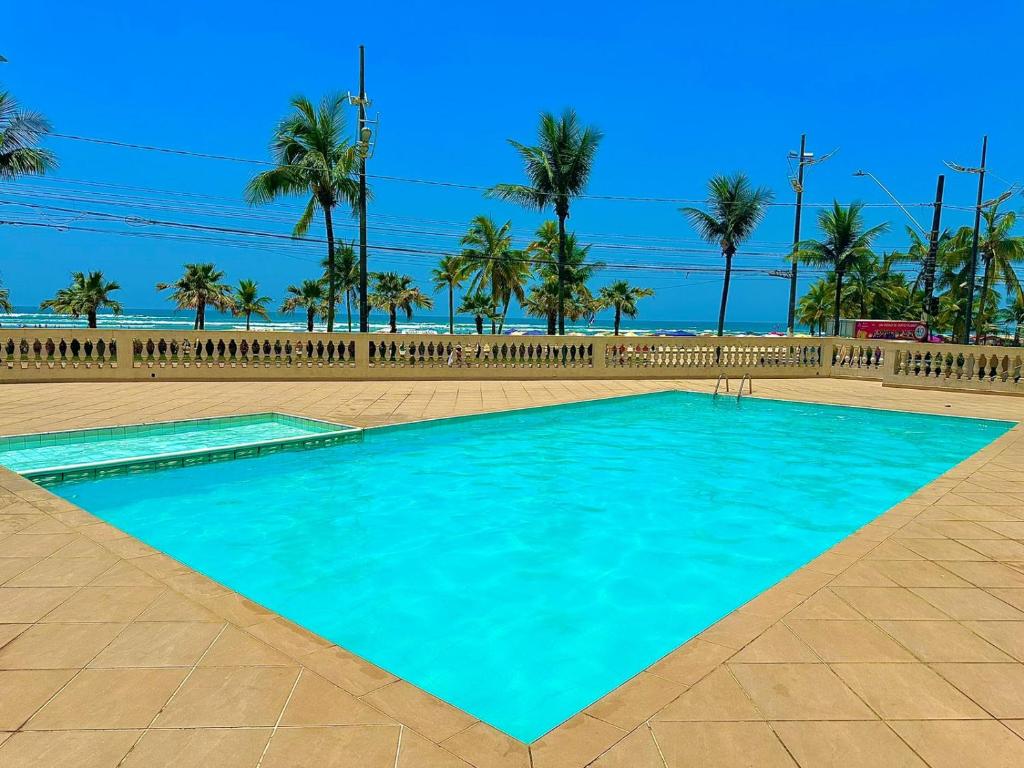 a swimming pool with palm trees and a beach at Apartamento frente ao mar com varanda e piscina in Praia Grande