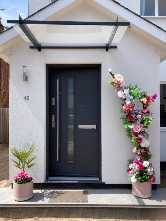 een zwarte deur op een wit huis met bloemen bij Cosy Modern Family Home Free Parking Garden in Londen