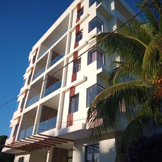 a tall white building with windows and a palm tree at Kensington Square Luxury Apartment in Flic-en-Flac
