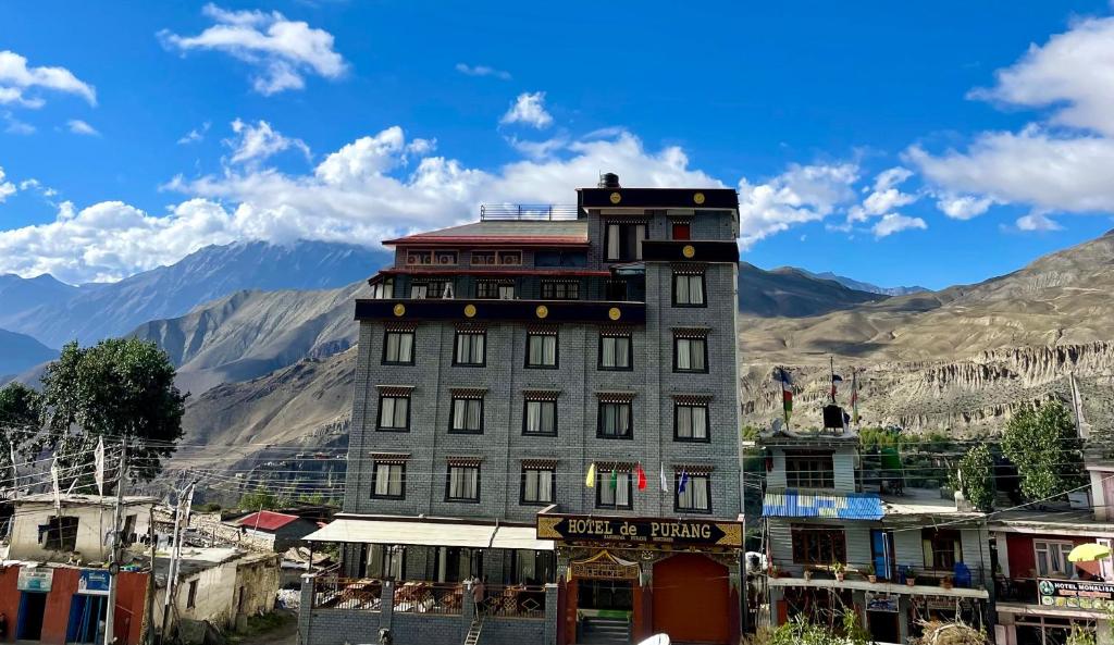 un grand bâtiment dans une ville avec des montagnes en arrière-plan dans l'établissement Hotel De Purang, à Muktināth