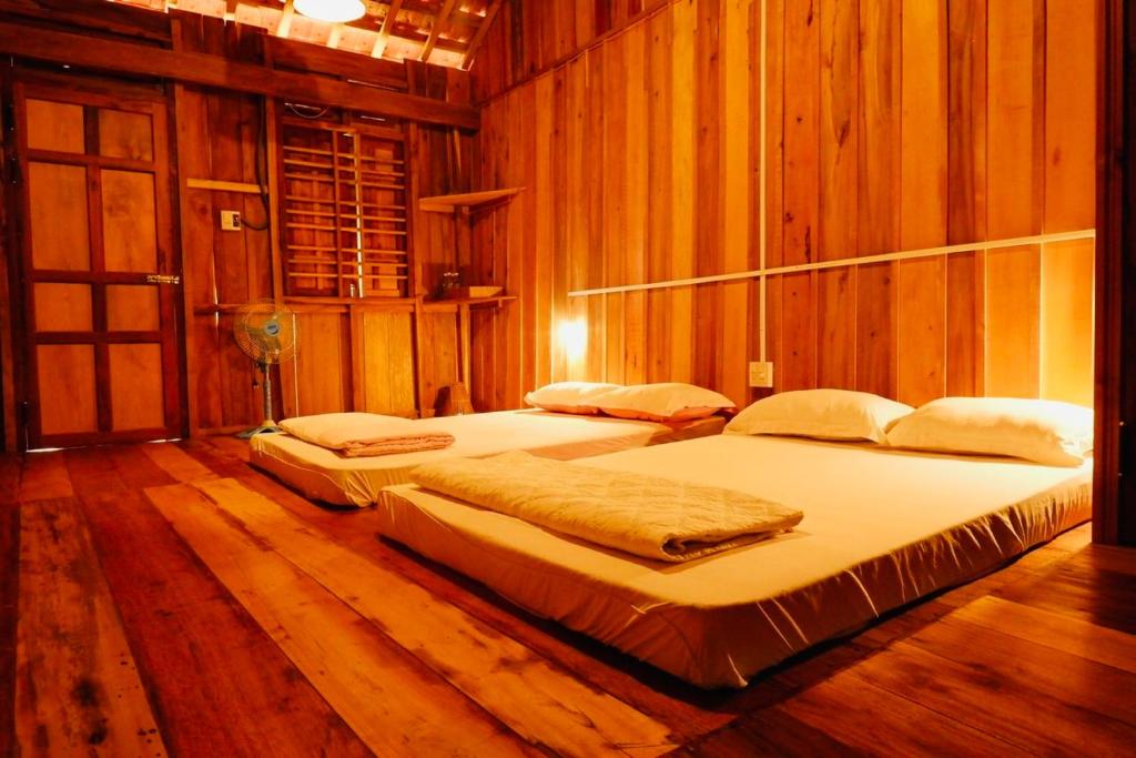 Homestay A Ngưi في De Dang (1): سريرين في غرفة بجدران خشبية وأرضيات خشبية