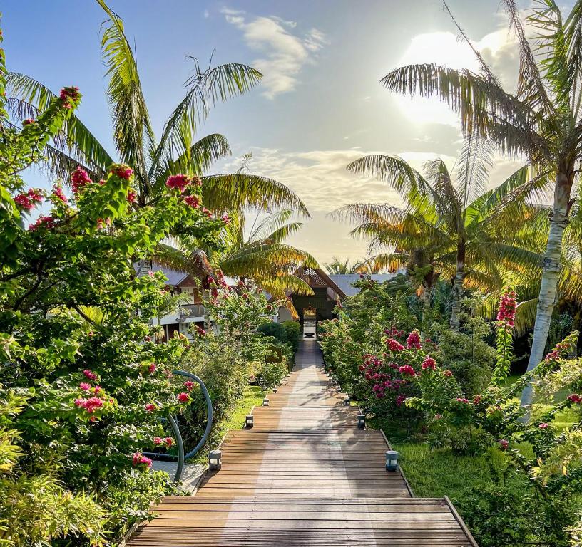 un sentier en bois traversant un jardin avec des fleurs et des palmiers dans l'établissement Akoya Hotel & Spa, à La Saline les Bains