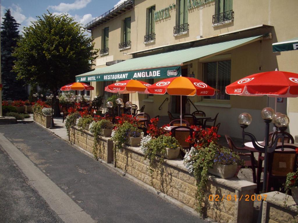 um café ao ar livre com mesas, guarda-sóis e flores em Hôtel Restaurant Anglade em Le Nayrac