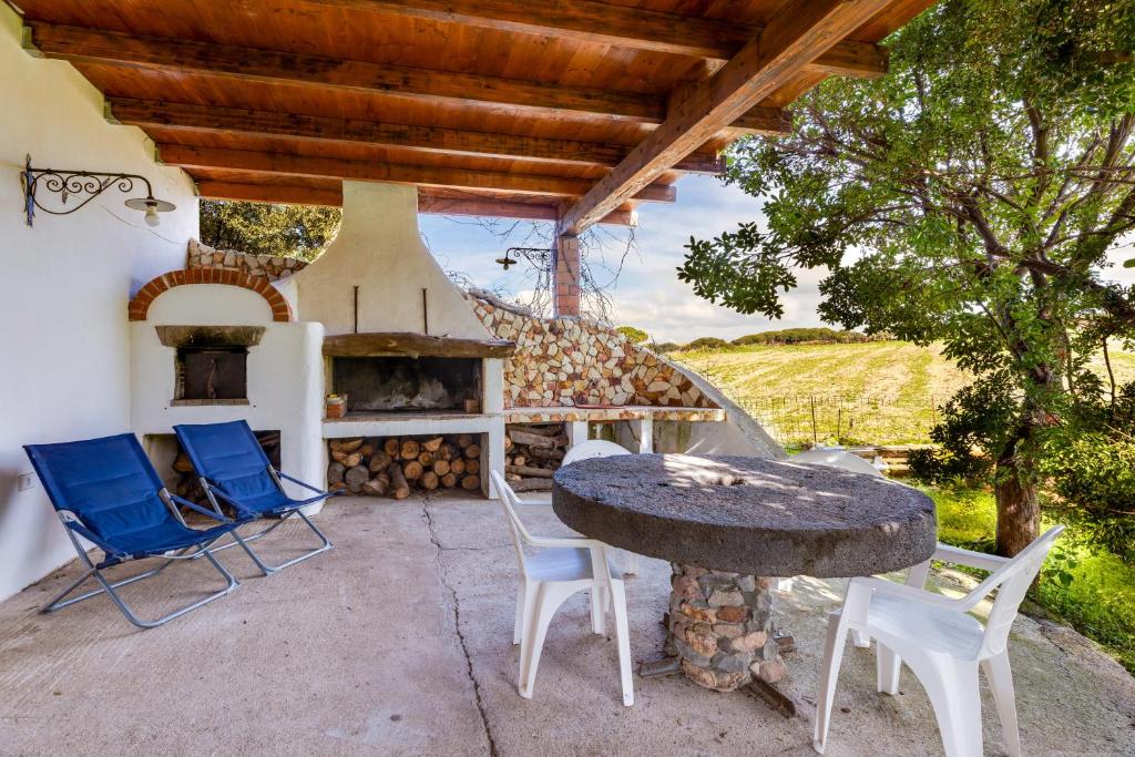 un patio con mesa, sillas y horno de piedra. en Villa due Archi, en S'Archittu