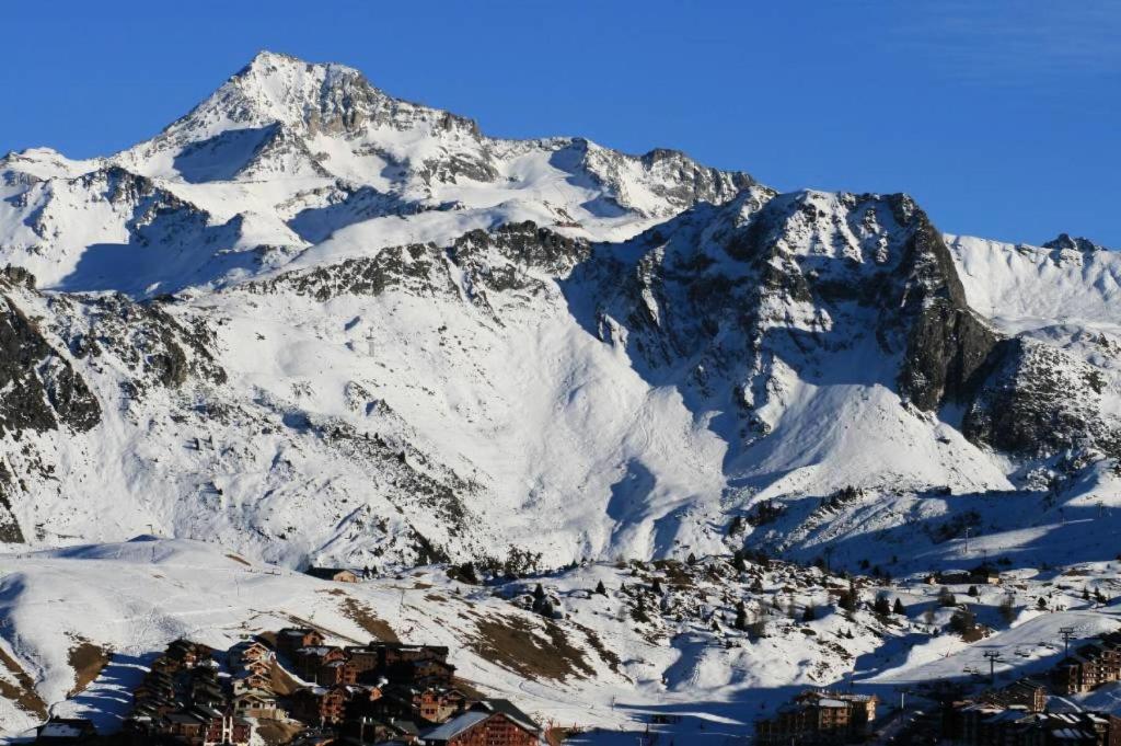 Une montagne enneigée avec une ville en face dans l'établissement Résidence Les Hauts Bois - maeva Home - Appartement 3 Pièces 6 Personnes - Sélection MAE-7828, à Aime La Plagne