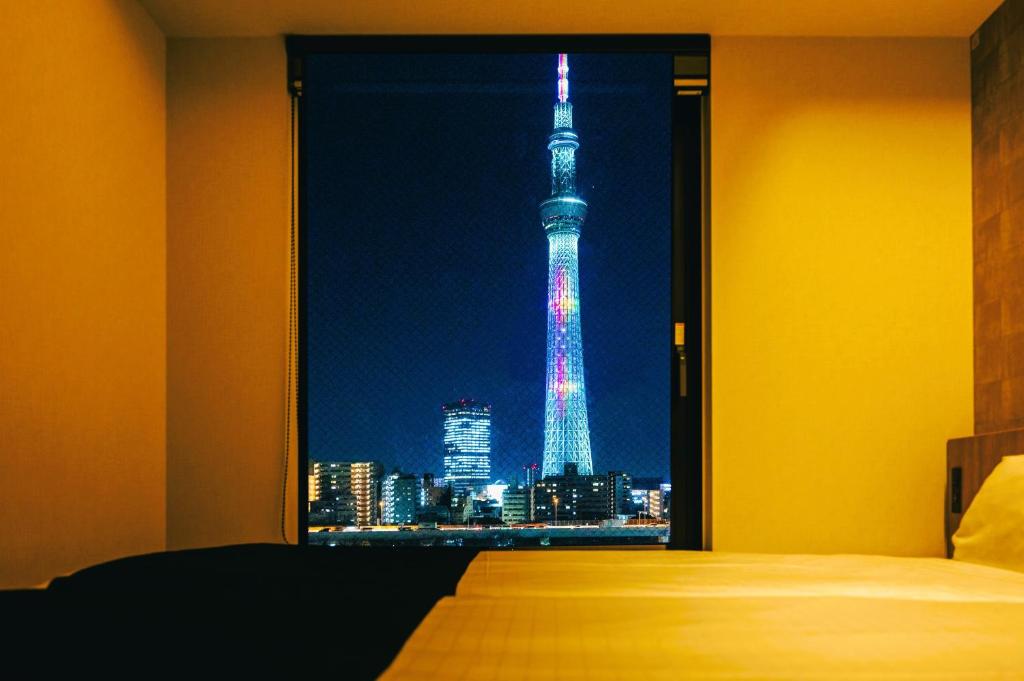 a bedroom with a view of the eiffel tower at night at stayme THE HOTEL Asakusa Riverside in Tokyo