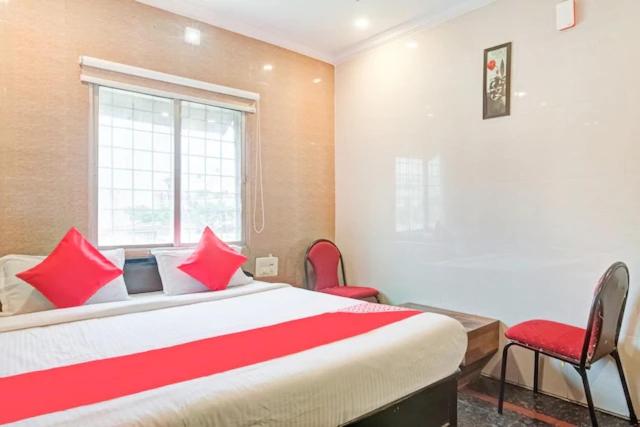 Schlafzimmer mit einem Bett mit roten Kissen und einem Fenster in der Unterkunft HOTEL TEJASRI RESIDENCY in Vijayawāda